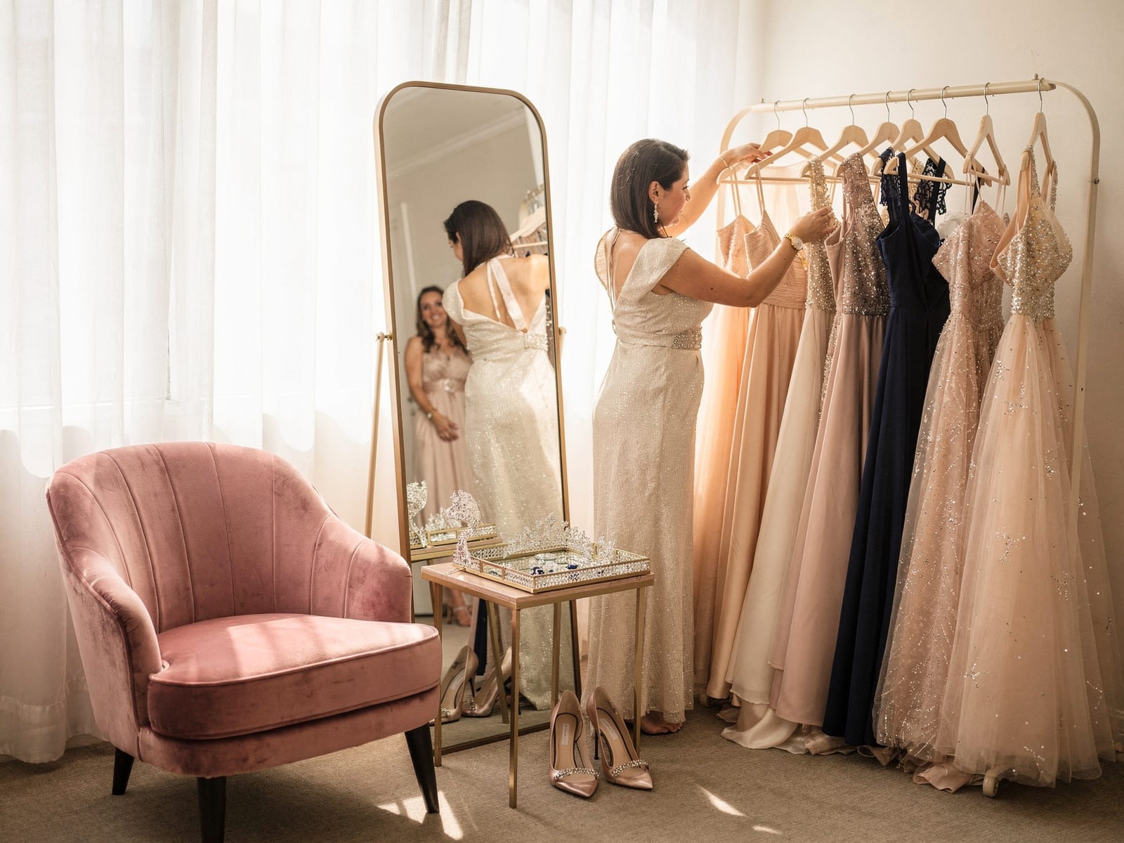 A welcoming boutique styling corner with a blush chair, mirror and a rack of gowns in soft daylight